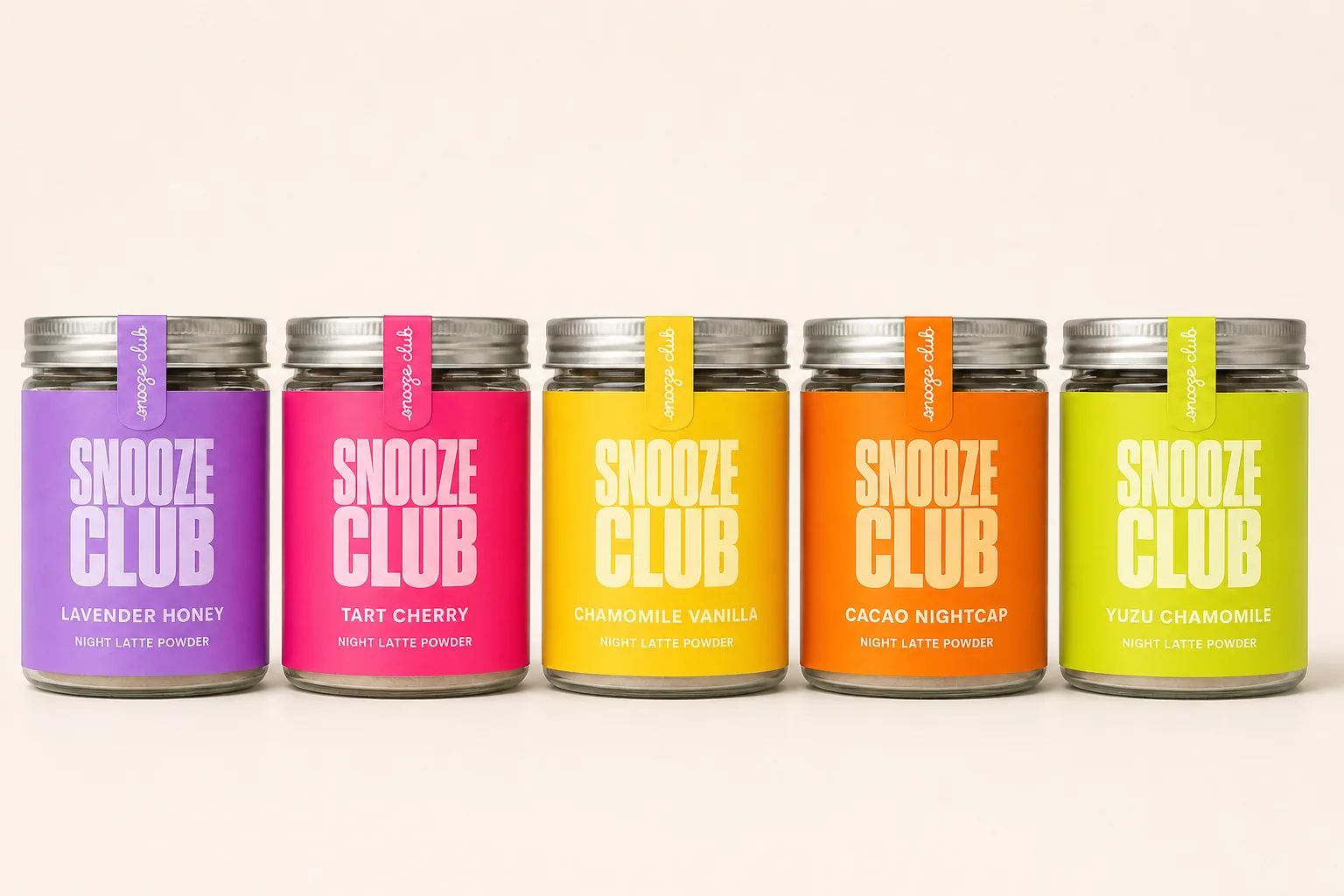 クリーム背景に並ぶSNOOZE CLUBの5色ガラス瓶 — ライラック・チェリーピンク・アンバー・オレンジ・シトロンのラベル、アルミ蓋とネックタグ